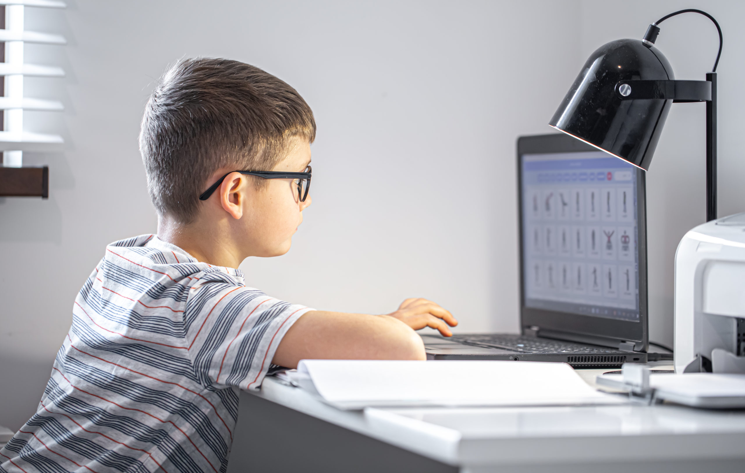 elementary-school-student-with-glasses-sits-table-with-laptop-does-his-homework-online-scaled