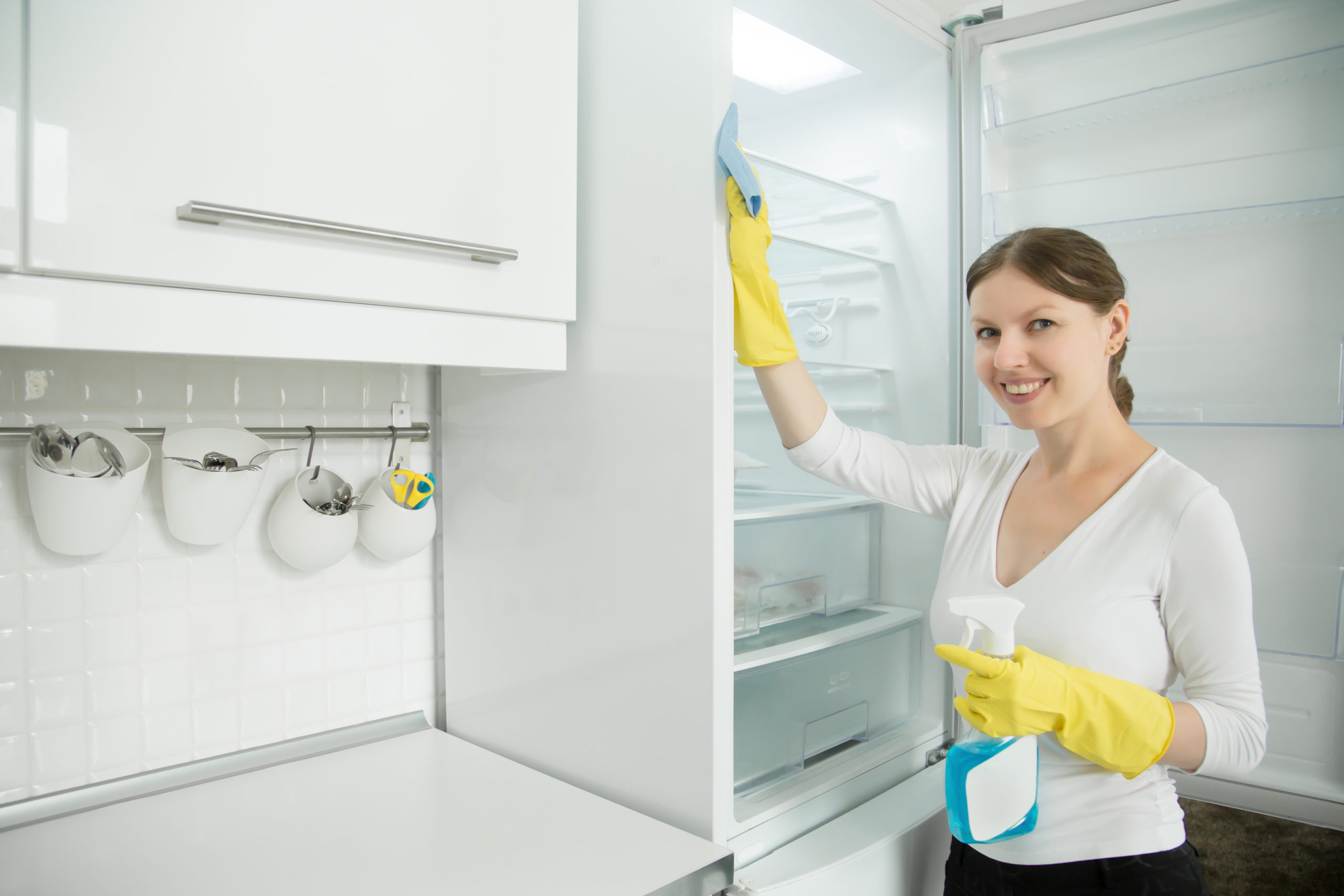 young-smiling-woman-wearing-rubber-gloves-cleaning-fridge-scaled